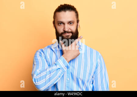 young handsome cheerful man with a palm on his beard looking at the camera over yellow background.isolated yellow background Stock Photo