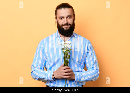 Happy handsome cheerful positive young man holding a bunch of flowers.isolated yellow background. studio shot. birthday, gift for wife. Stock Photo