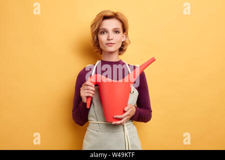 Photo of awesome florist with watering can in hand looking at the camera, she is going to water flowers. lifestyle, hobby, job, profession, free time, Stock Photo