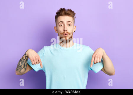 bearded handsome man indicates down as shows something, , isolated over blue concrete wall.close up portrait. studio shot.body language. Stock Photo