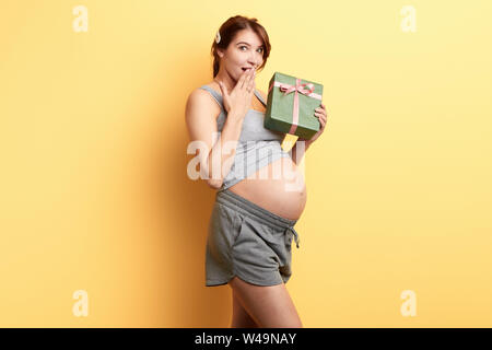 surprised excited girl with a palm on her mouth has received a gift on her Birthday from boyfriend. love, pleasant moment. isolated yellow background. Stock Photo