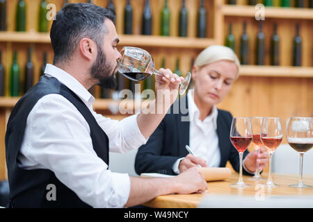 Young elegant sommelier tasting red wine from one of glasses Stock Photo