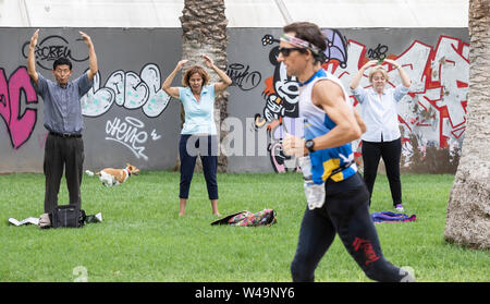 Las Palmas, Gran Canaria, Canary Islands, Spain, 21st July, 2019. Pleasure and pain. A competitor runs past a group of people practicing Falun Dafa / Falun Gong during the last hour of a 24 hour race for relay teams and individuals on a 1km circuit in Las Palmas on Gran Canaria. PICTURED: Winner of the individual race, Eduardo Cebrián, who ran 220km in 24 hours. Credit:Alan Dawson/Alamy Live News Stock Photo