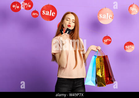 girl kissing her credit cards, dicounts while doing shopping. woman has recieved a card after shopping, girl has bought many stylish clothes with disc Stock Photo