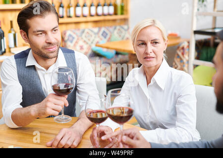 Group of colleagues in formalwear discussing quality of red wine Stock Photo