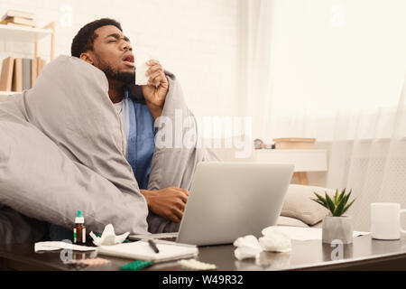 Ill man suffering from rhinitis working on couch with laptop Stock Photo