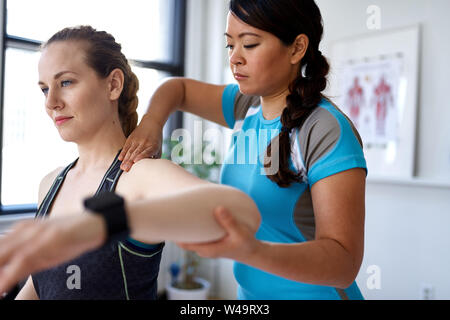 Chinese woman physiotherapy professional giving a treatment to an attractive blond client in a bright medical office Stock Photo