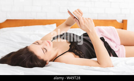 Happy woman lying on bed reading text message Stock Photo