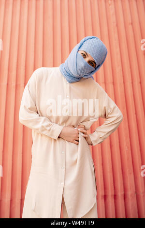 Young muslim female with face hidden behind blue hijab looking at you Stock Photo