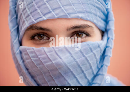 Beautiful eyes of young muslim woman with her face hidden behind blue hijab Stock Photo