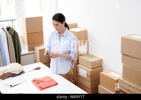 Young manager of online shop office taking photo of folded red pullover Stock Photo