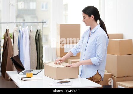 Young manager of online shop packing box with casualwear Stock Photo