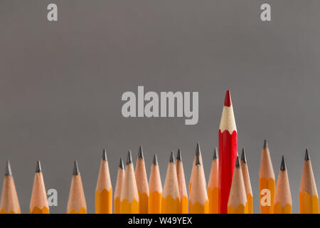 One red pencil sticking out of similars crowd on gray background Stock Photo