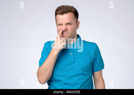 Young caucasian man in blue shirt picking in his nose. Stock Photo