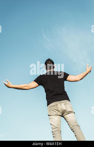 Man looking at the sky and screaming with open arms. Man with background of a clear sky with copy space top. Stock Photo