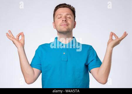 Young handsome man in blue t-shirt relaxing and smiling with eyes closed doing meditation gesture Stock Photo