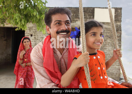 Indian man pushing his daughter on the swing Stock Photo