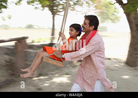 Man pushing his daughter on the swing Stock Photo