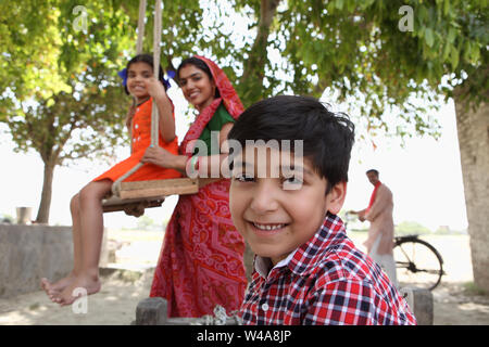 Boy smiling with his mother pushing his sister on swing Stock Photo