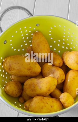 Potatoes, washed, in a bright green metal colander. On a white wood background Stock Photo