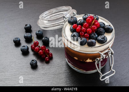 Layered cake dessert in jar, chocolate and fruit cream, decorated with berries. Stock Photo