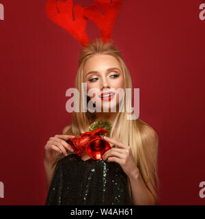 Beautiful blonde girl in a New Year's image with Christmas bells around her neck and deer horns on her head. Beauty face with festive makeup. Photo ta Stock Photo
