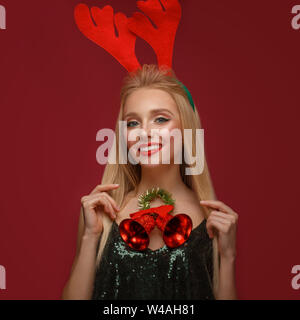 Beautiful blonde girl in a New Year's image with Christmas bells around her neck and deer horns on her head. Beauty face with festive makeup. Photo ta Stock Photo