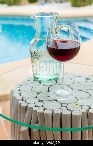 Carafe of water and glass wine with swimming pool in background Stock Photo