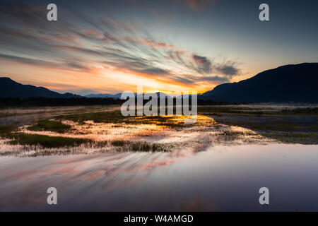 Spectacular sunrise over marshlands with mountain range in background Stock Photo