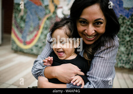 Mother hugging daughter & laughing in front of mural Stock Photo