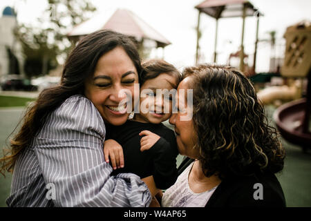 Mother and grandmother hugging daughter in park Stock Photo