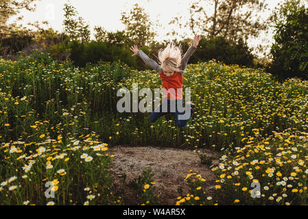 Young boy jumping in field of flowers with backlight Stock Photo
