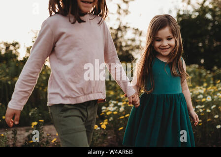 Smiling sisters walking through a field of flowers in spring Stock Photo