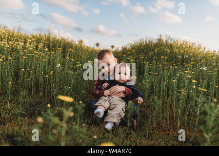 Portrait of brothers sitting in a field of flowers smiling Stock Photo