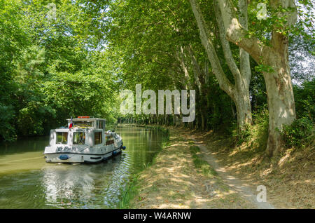 A pleasure boat cruising along the Canal du Midi, France, between the avenue of plane trees that line both sides of the canal Stock Photo