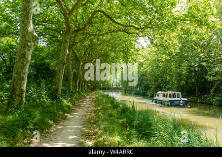 A pleasure boat cruising along the Canal du Midi, France, between the avenue of plane trees that line both sides of the canal Stock Photo