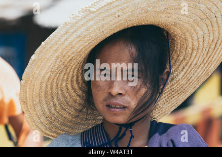 Indein, Myanmar - March 2019: portrait of a young Burmese woman in a big straw hat and tanaka on her face Stock Photo