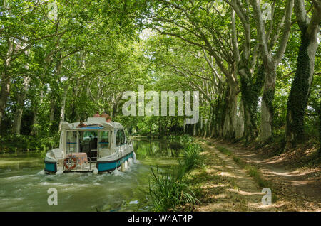 A pleasure boat cruising along the Canal du Midi, France, between the avenue of plane trees that line both sides of the canal Stock Photo