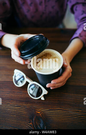 Female hands with a cup of cappuccino with thick foam in black takeaway paper cup. Stock Photo