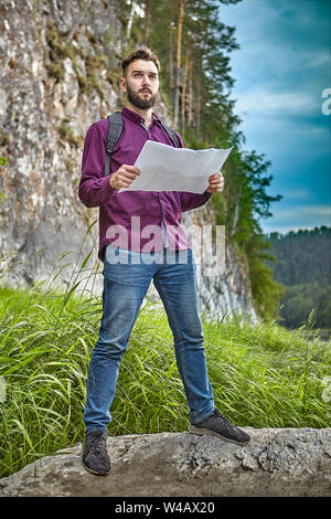 Adventure in the wild, a young man is engaged in hiking, or ecotourism in the ecological environment of a mountain river, he orients himself on the te Stock Photo