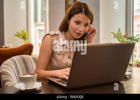 Young beautiful interested woman works on laptop in cafe Stock Photo