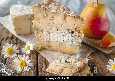A slice of blue aged Stilton cheese on a wooden table. Cheese is served with a beautiful ripe pear. The quality of farmers ' agricultural products. De Stock Photo