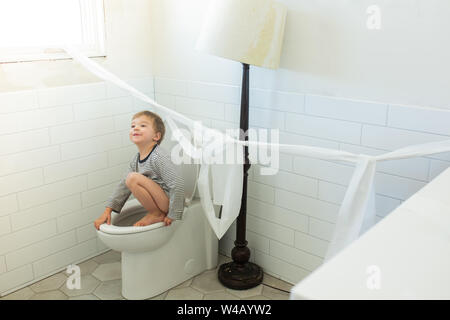 Toddler making mess in bathroom with toilet paper hung on wall Stock Photo