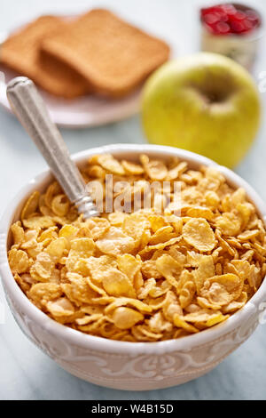 Cornflakes bowl, apple and bread in the background. Breakfast concept Stock Photo