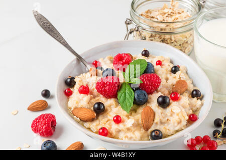 oatmeal porridge with fresh berries, nuts, honey, mint in a bowl with glass of milk for healthy diet breakfast. close up Stock Photo