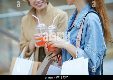 Close-up of positive ladies with shopping bags drinking sweet cocktails and chatting in mall Stock Photo