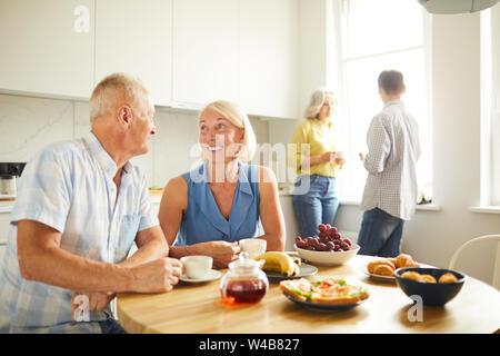 Portrait of happy mature couple looking at each other tenderly while siting at kitchen table in sunlight, copy space Stock Photo