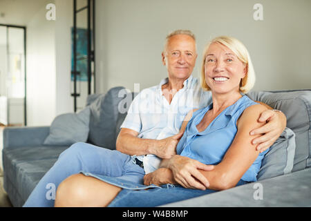 Portrait of smiling mature couple posing sitting on sofa at home, copy space Stock Photo
