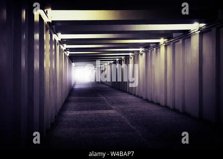 An image of light at the end of a underground concrete tunnel. A long concrete tunnel with lanterns in the city underground. Underpass. Stock Photo