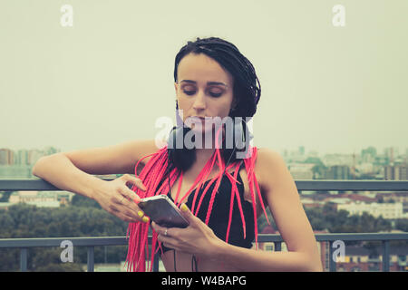 Trendy teenage girl listening to music on headphones. Rock style. Modern generation. woman with a piercing on her face looking at the smartphone. Sad Stock Photo